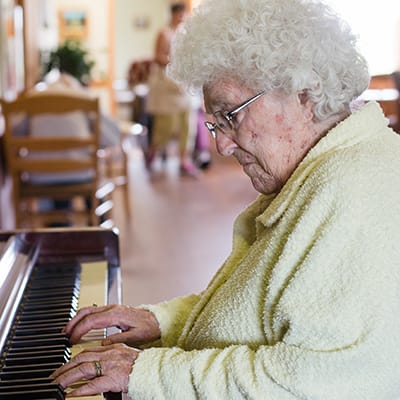 An elderly woman playing piano in a cozy common area
