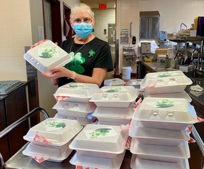 Staff member presenting food packages in a kitchen area