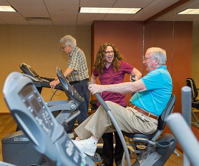 Residents exercising with staff assistance in a gym