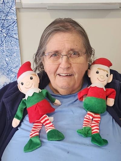 A smiling resident holding two festive elf dolls