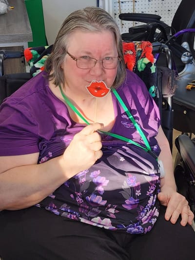 Resident playfully holding a lips prop in activity room