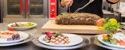 Chef slicing a roast with plated meals in the foreground