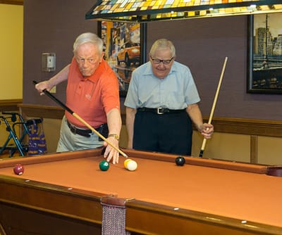 Two seniors playing pool in an activity room.