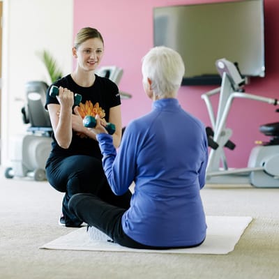 A staff member assisting a resident with weights in a fitness area