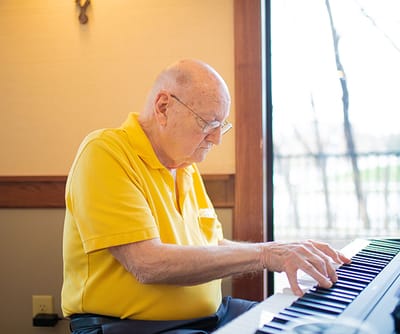 An elderly man playing piano in a common area