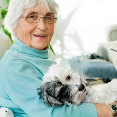 An elderly woman smiling while holding a small dog