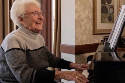 Senior resident playing piano and smiling