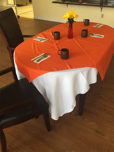 Dining table set with orange tablecloth and flower vase.