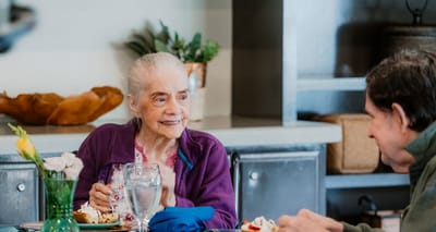 A senior woman enjoying a meal with a companion.