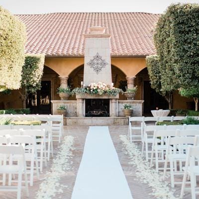 Outdoor wedding setup with white chairs and floral decor.