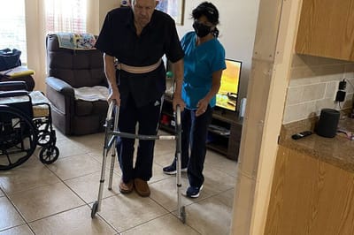 Staff assisting a resident with a walker in a living space.