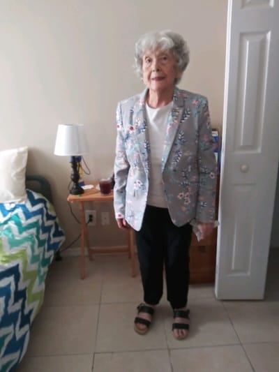 Elderly woman in a floral blazer standing in a room.