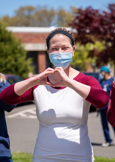 Staff member making a heart gesture outdoors.