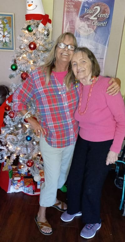 Resident and staff member celebrating by a decorated Christmas tree.
