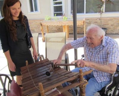Resident and staff member engaging with musical instrument outdoors.