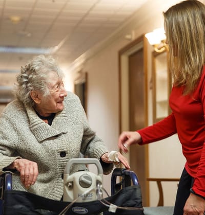 Staff assisting an elderly resident in a hallway.