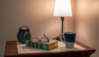 A bedside table with books, clock, and a mug