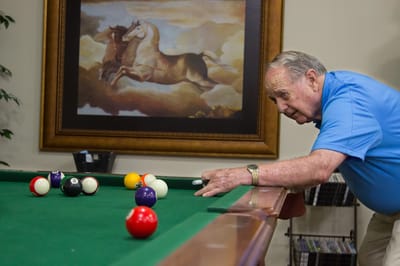 Senior playing billiards in an interior activity area.