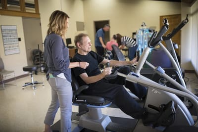 Staff assisting a resident with exercise equipment.