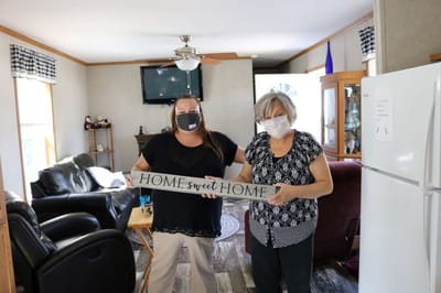 Two women holding a decorative sign in a cozy living room.