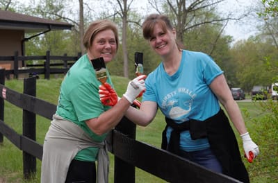 Two women painting a fence outdoors together.