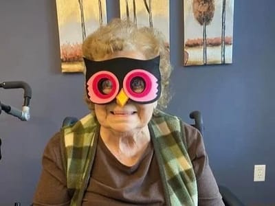Elderly woman wearing oversized owl glasses and smiling.