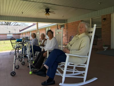 Residents sitting on rocking chairs in outdoor area.