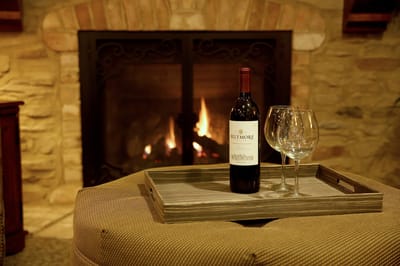 Wine and glasses on a tray by a fireplace.