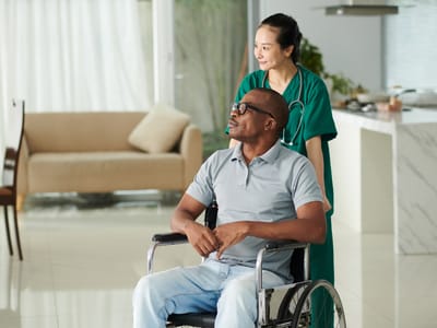 Caregiver assisting a resident in a wheelchair indoors.