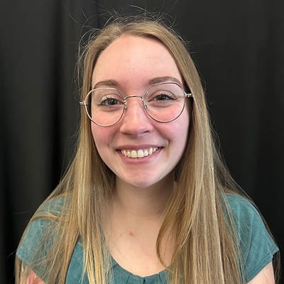 Smiling woman with glasses in front of black backdrop.