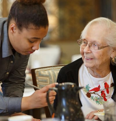Staff assisting a resident in a dining setting.