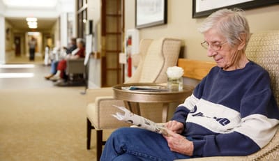 Senior resident reading a newspaper in a common area.