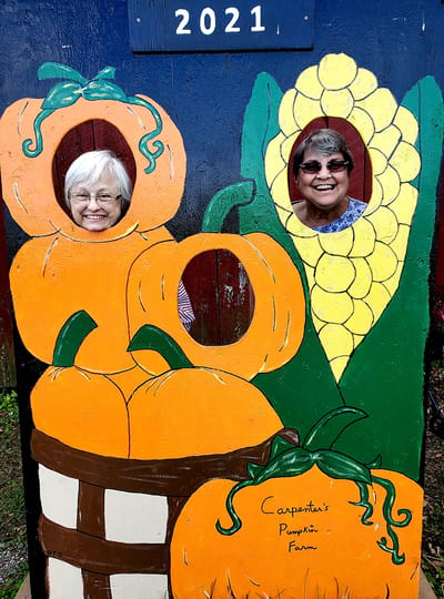 Two women smiling through pumpkin cutouts