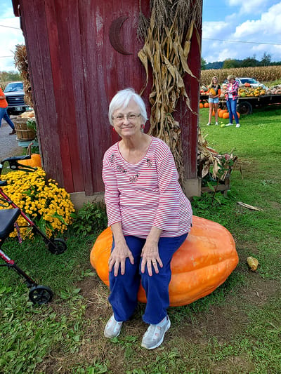 Senior woman sitting on a large pumpkin outdoors