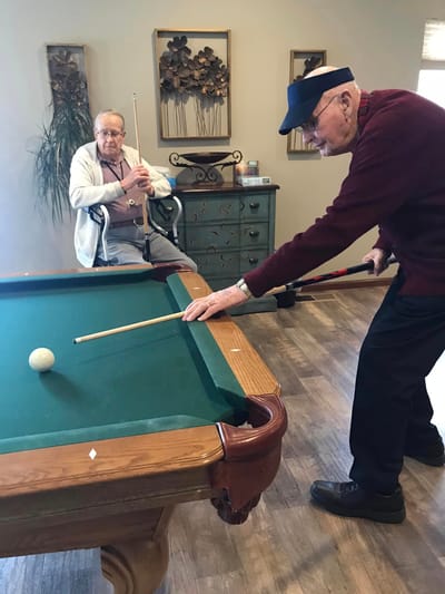 Two seniors playing pool in a common area.