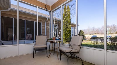 Screened-in porch with chairs and small table.