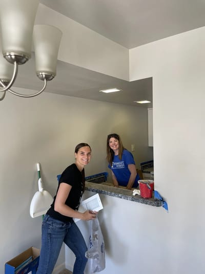 Two staff members smiling in a clean facility kitchen.
