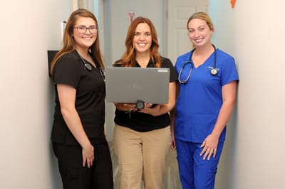 Three staff members posing in a hallway with a laptop.