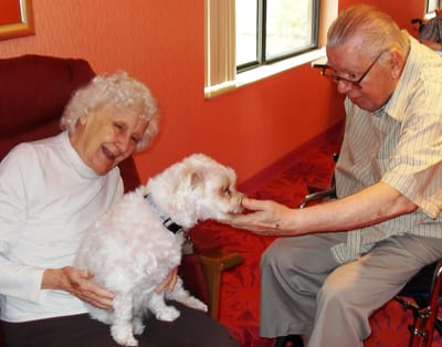 Senior residents enjoying time with a dog indoors.