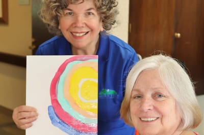 Two women smiling while showcasing colorful artwork.