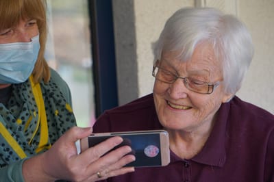 Staff member shows a smartphone to senior resident.