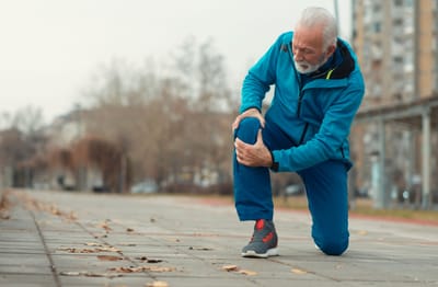 Senior man exercising outdoors, holding his knee.