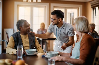 Residents enjoying a meal with staff in a dining area.