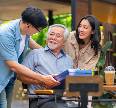A senior man receiving a gift outdoors from family members