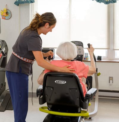 Staff assisting a resident on exercise equipment.