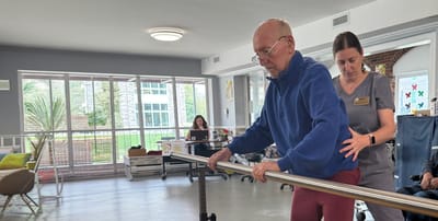 Resident participating in physical therapy with staff assistance.