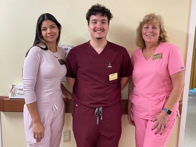 Three staff members in nursing uniforms posing together.