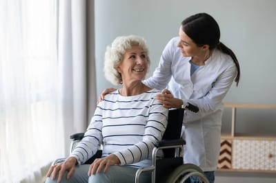 Caregiver assisting a smiling resident in a wheelchair.