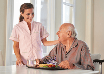 A caregiver assists an elderly man during mealtime.
