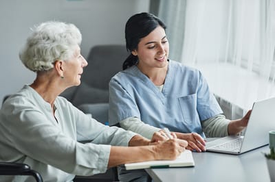 Caregiver assisting a senior resident with a laptop.